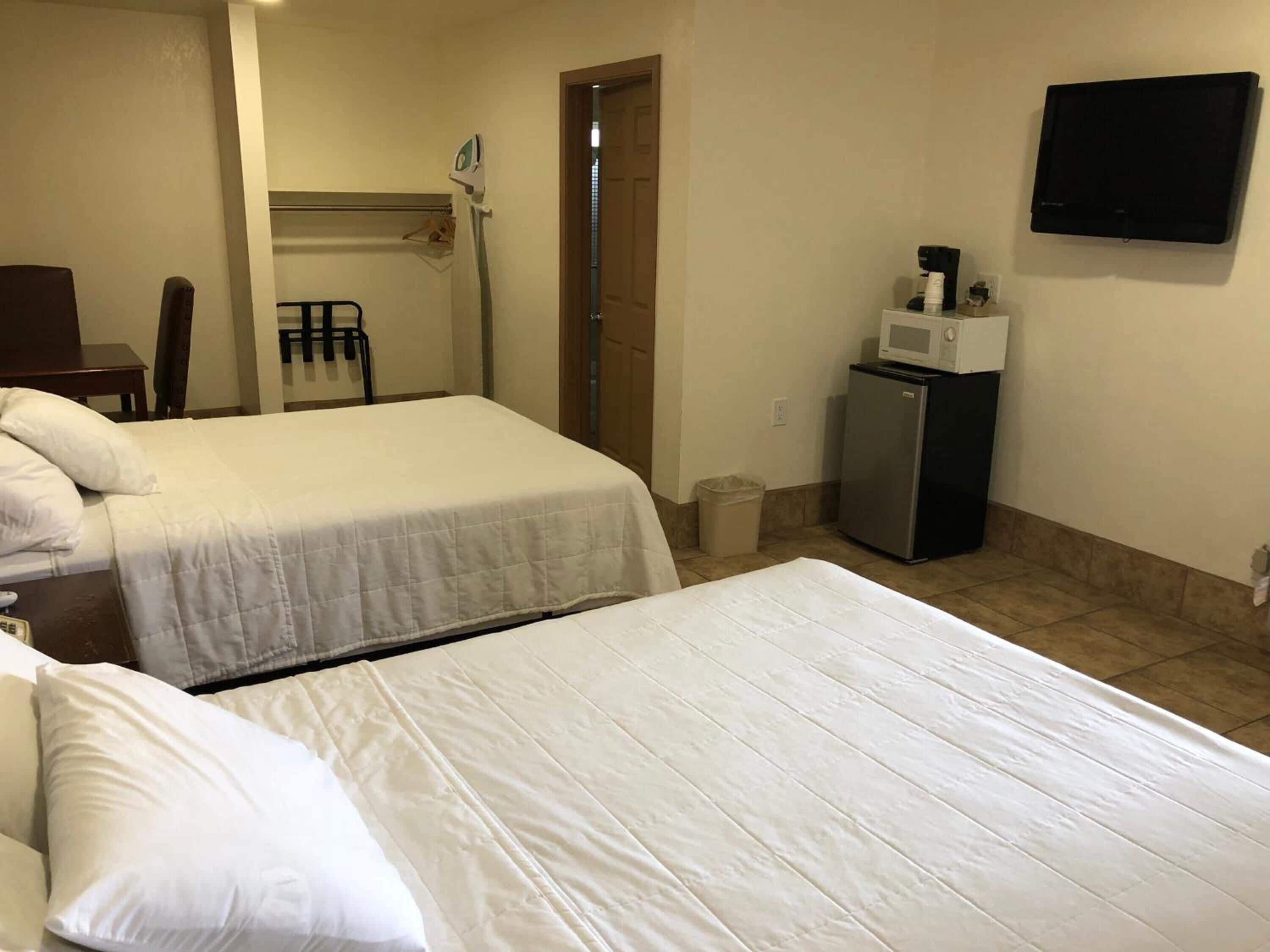 A hotel room with two beds, a desk, a chair, a microwave, a refrigerator, and a TV.
