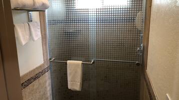 A shower area with a glass door, a towel rack with two towels, and a tiled floor.