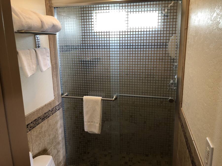 A shower area with a glass door, a towel rack with two towels, and a tiled floor.