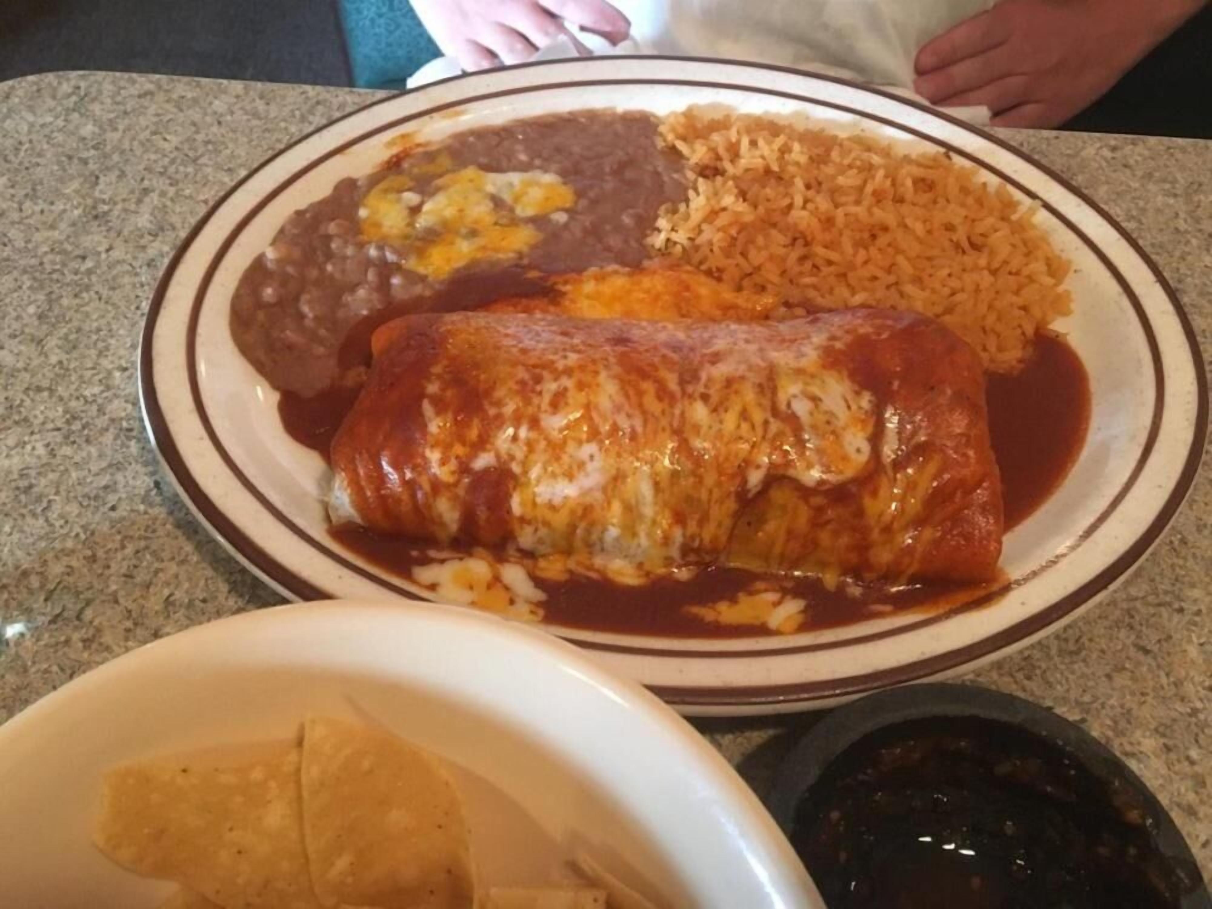 A plate with a rolled dish, beans, rice, and a bowl of chips.