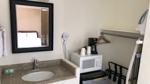 A bathroom with a sink, mirror, hairdryer, microwave, and a small refrigerator. - Topper Motel (Taft)