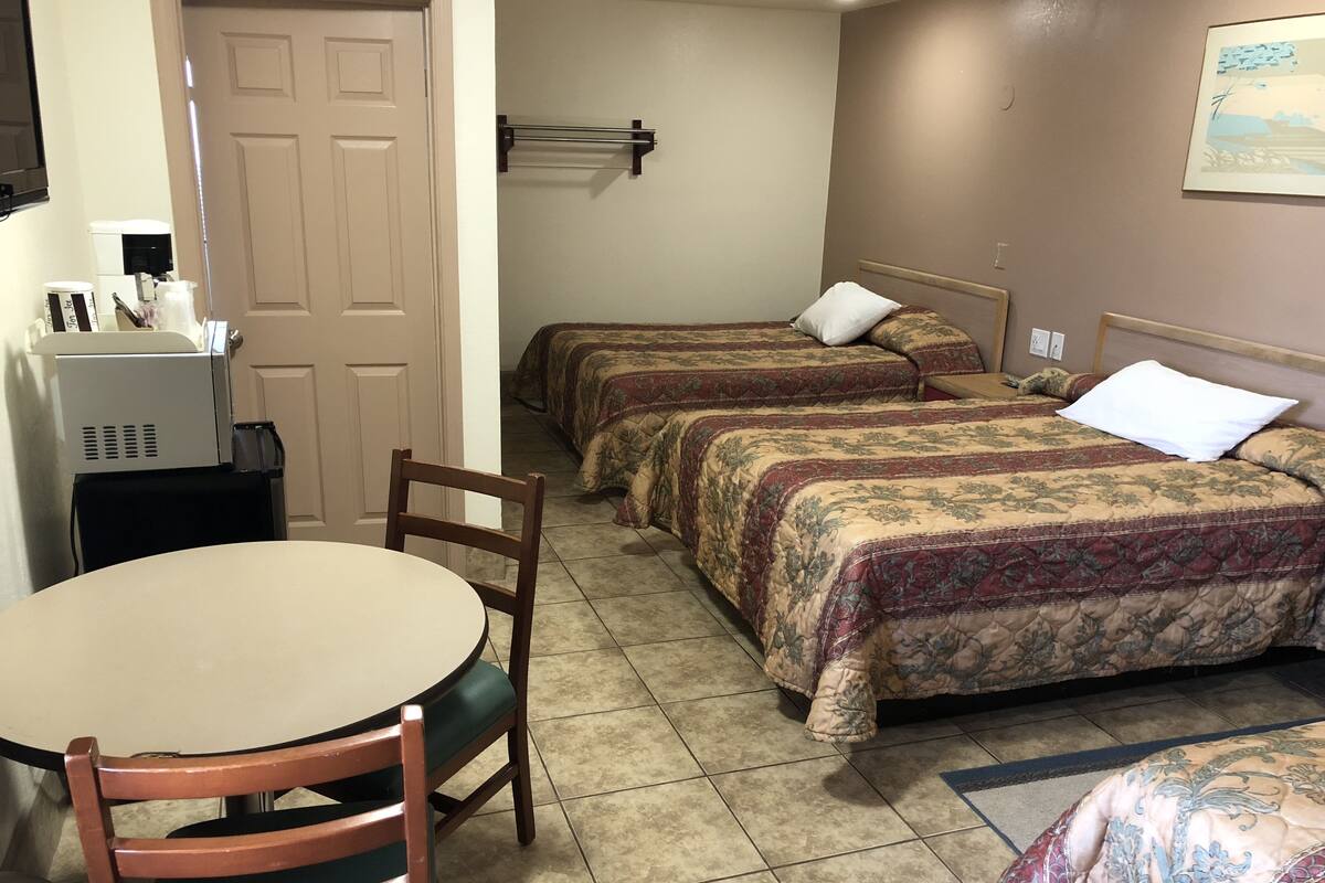 A hotel room with two beds, a small table, a chair, a desk with a computer, and a door.