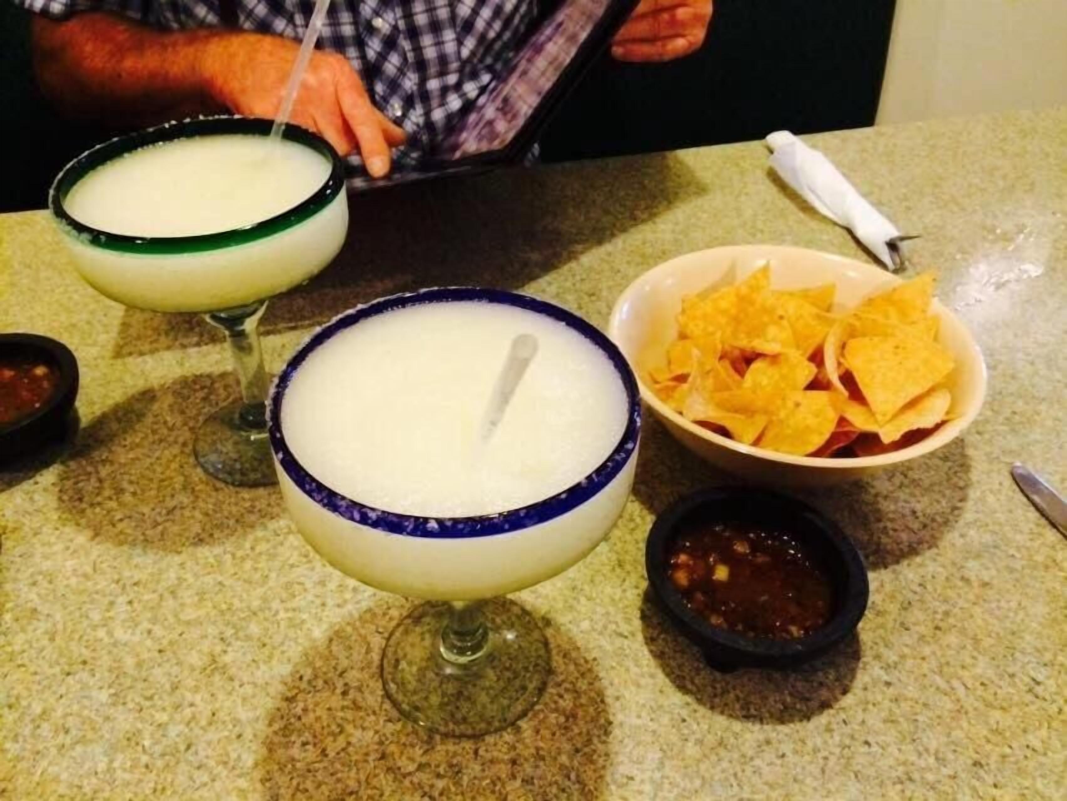 A table with two margaritas in glasses, a bowl of tortilla chips, and two small bowls of salsa.