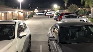 A parking lot at night with several cars parked, illuminated by street lamps. - Topper Motel (Taft)