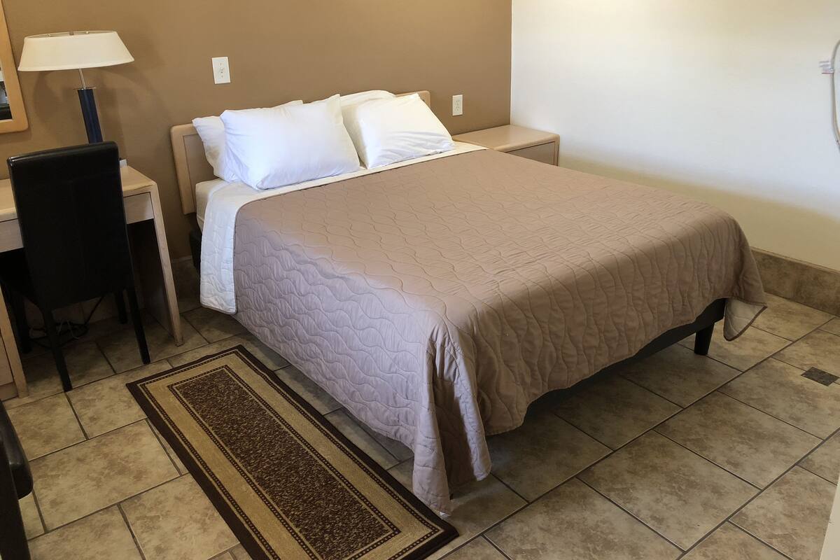 A neatly arranged bedroom with a bed, bedside table, lamp, chair, and a rug.
