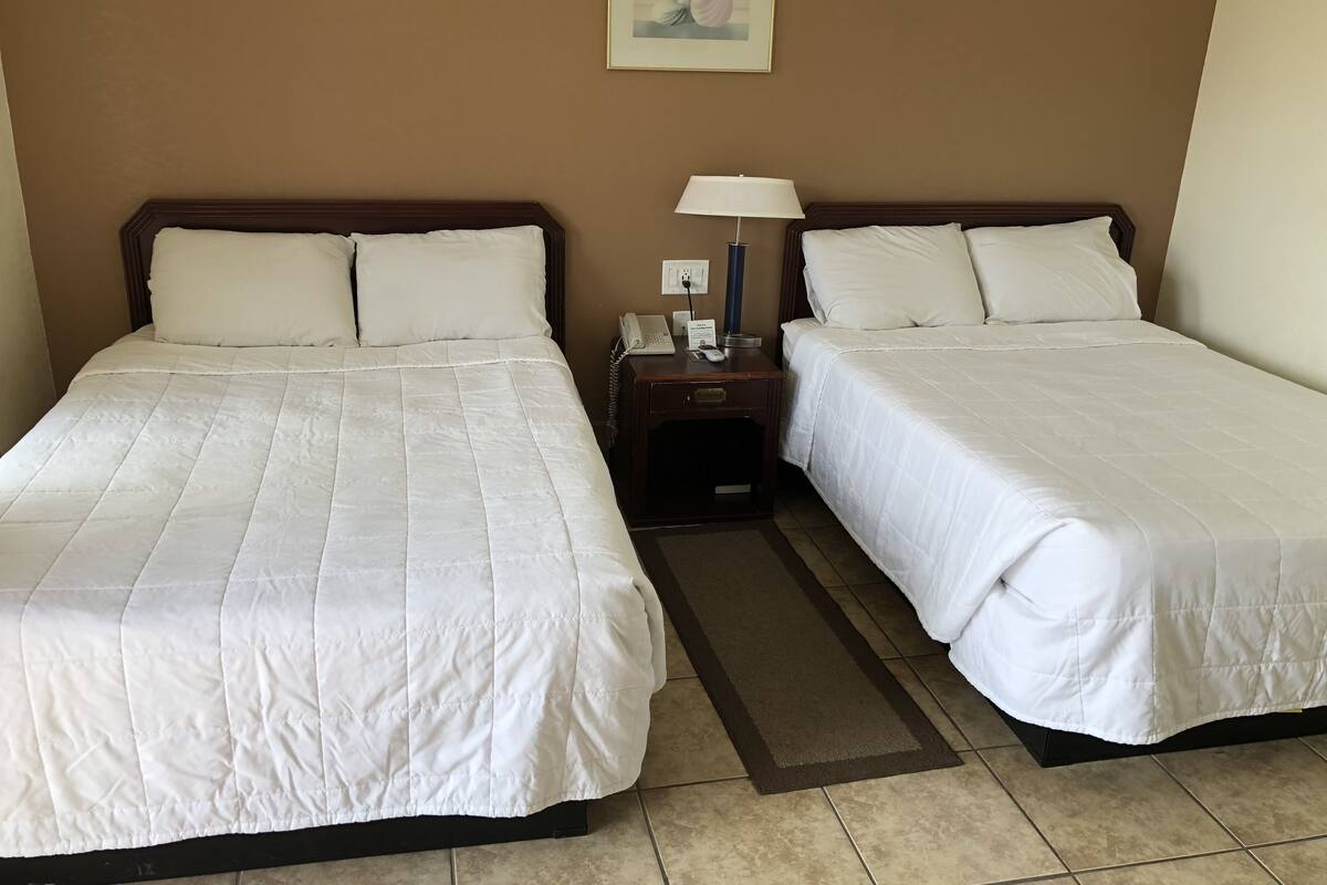 A hotel room with two beds, a nightstand with a lamp, a phone, and a painting on the wall.