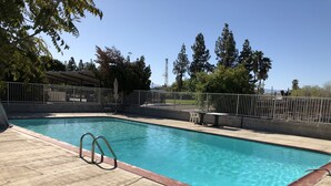 A rectangular swimming pool with a metal ladder, surrounded by a concrete deck and a metal fence. - Topper Motel (Taft)