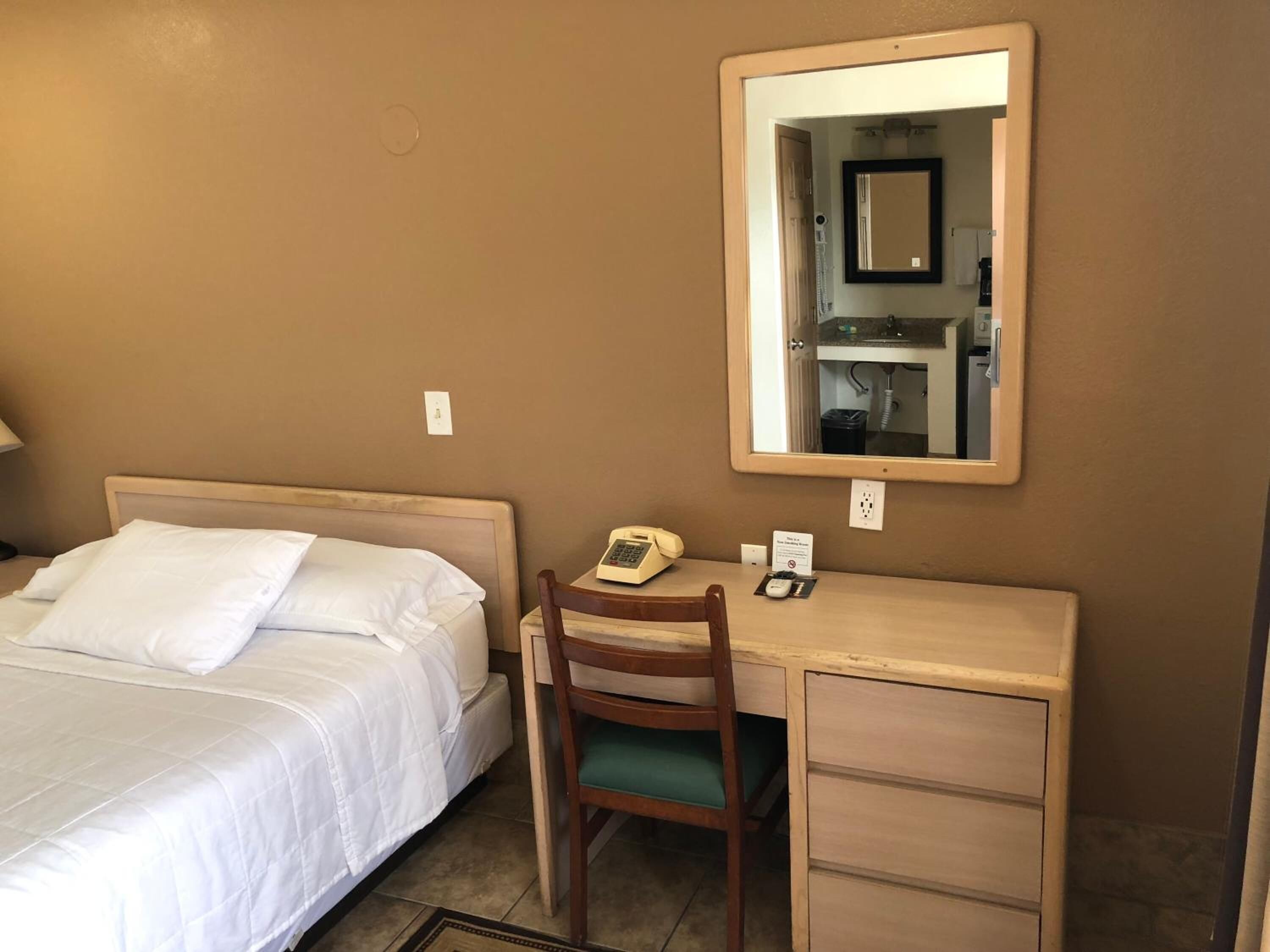 A hotel room with a bed, a desk, a chair, a telephone, and a mirror.