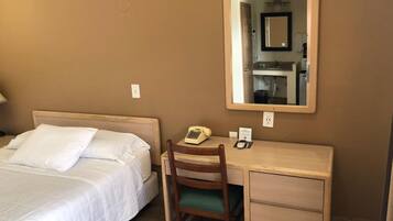 A hotel room with a bed, a desk, a chair, a telephone, and a mirror.