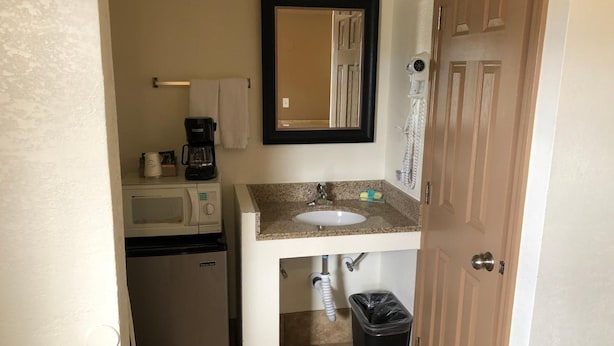 A compact bathroom with a sink, mirror, towel rack, coffee maker, microwave, and trash bin. - Topper Motel (Taft)