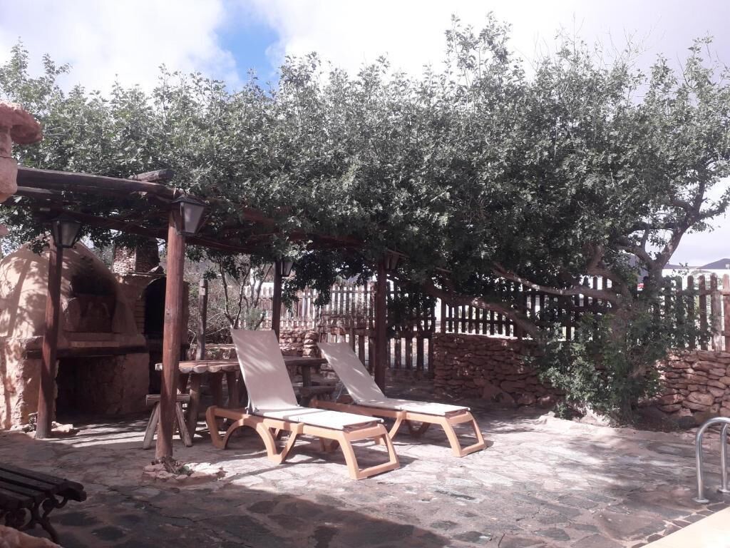 A patio area with two wooden lounge chairs, a stone table, and a pergola structure.