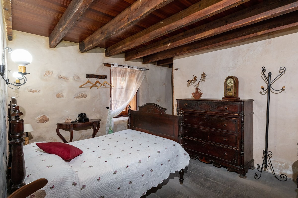 A bedroom with a wooden bed, a dresser, a lamp, and a wall clock.