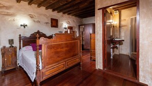 Une chambre à coucher avec un lit en bois, une table de chevet, une commode et une salle de bain visible à travers une porte ouverte.