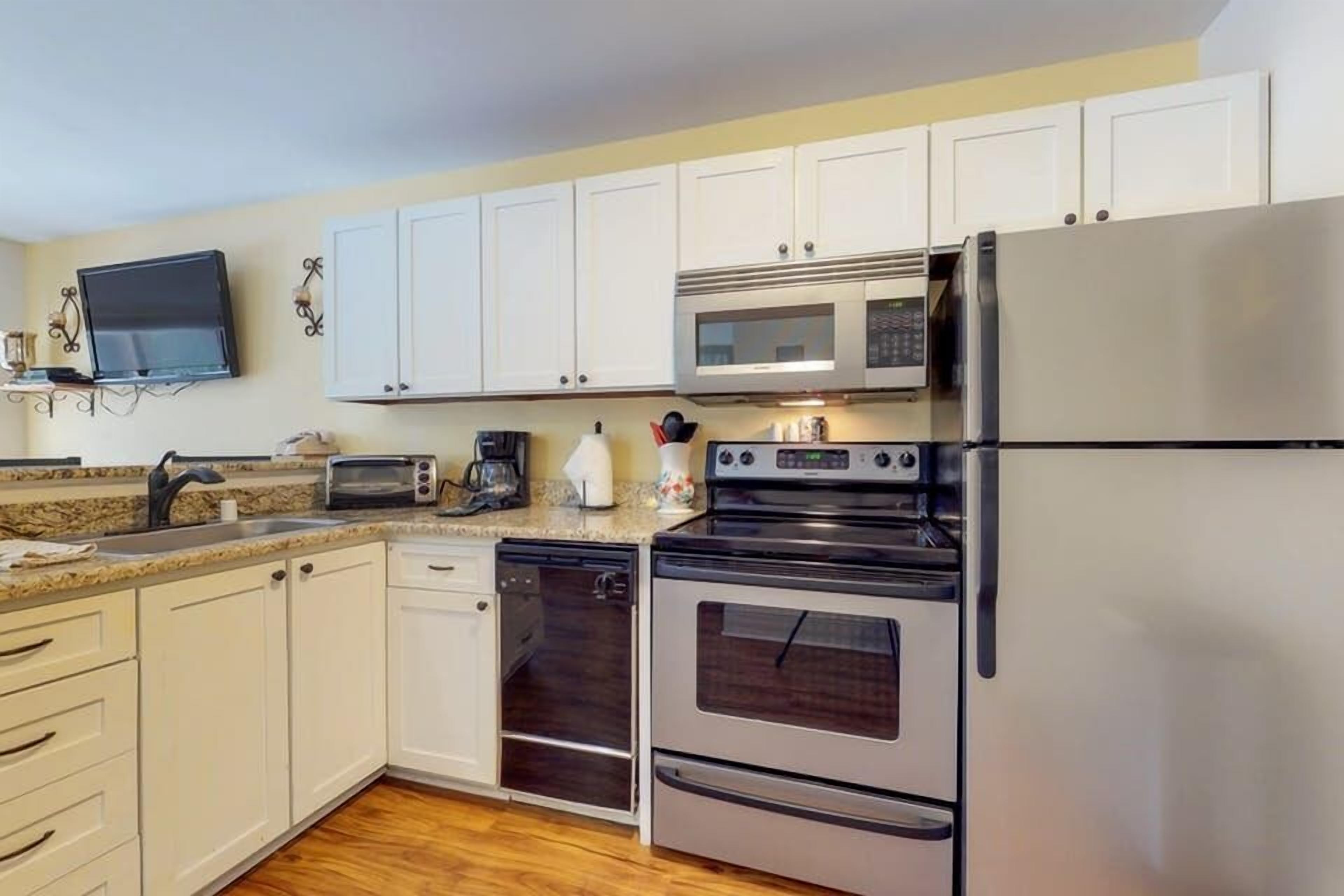 A modern kitchen with white cabinets, a stainless steel refrigerator, a microwave, an oven, and a dishwasher.