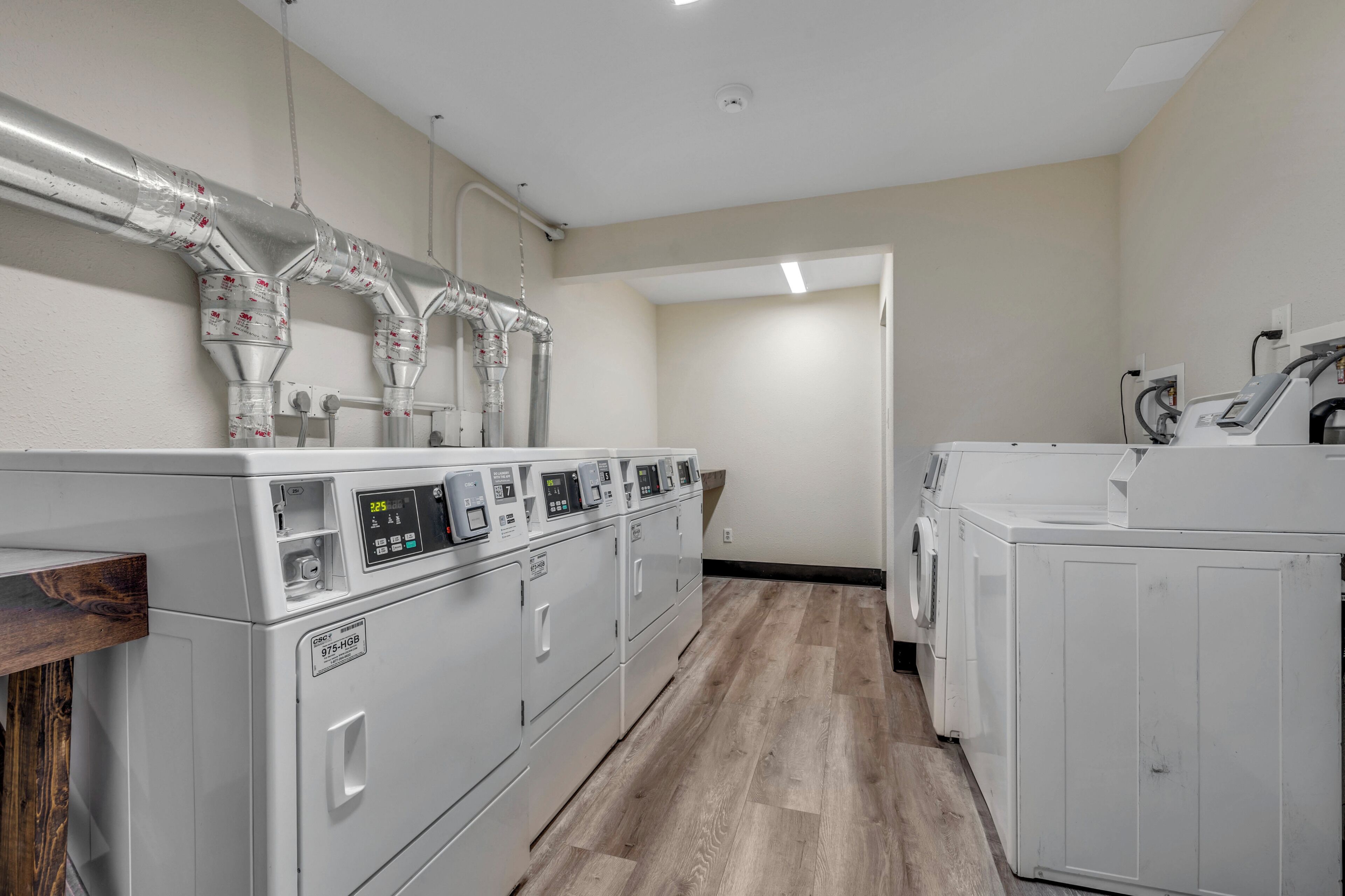 Une buanderie équipée de plusieurs machines à laver et de plusieurs sèche-linge, avec un plancher en bois et un système de ventilation mural.