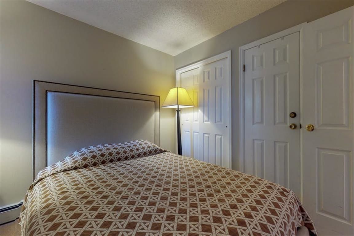 A bedroom with a bed, a nightstand, a lamp, and a door.