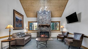 A cozy living room with a stone fireplace, leather sofas, and a flat-screen TV mounted on the wall. - Wildwood Lodge Downtown Condos with Hot Tub (Breckenridge)