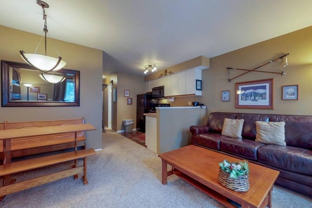 A living room with a wooden bench, a coffee table, a leather sofa, and a kitchen in the background.
