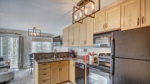 A modern kitchen with wooden cabinets, a granite countertop, stainless steel appliances, and a large window providing natural light. - Wildwood Lodge Downtown Condos with Hot Tub (Breckenridge)