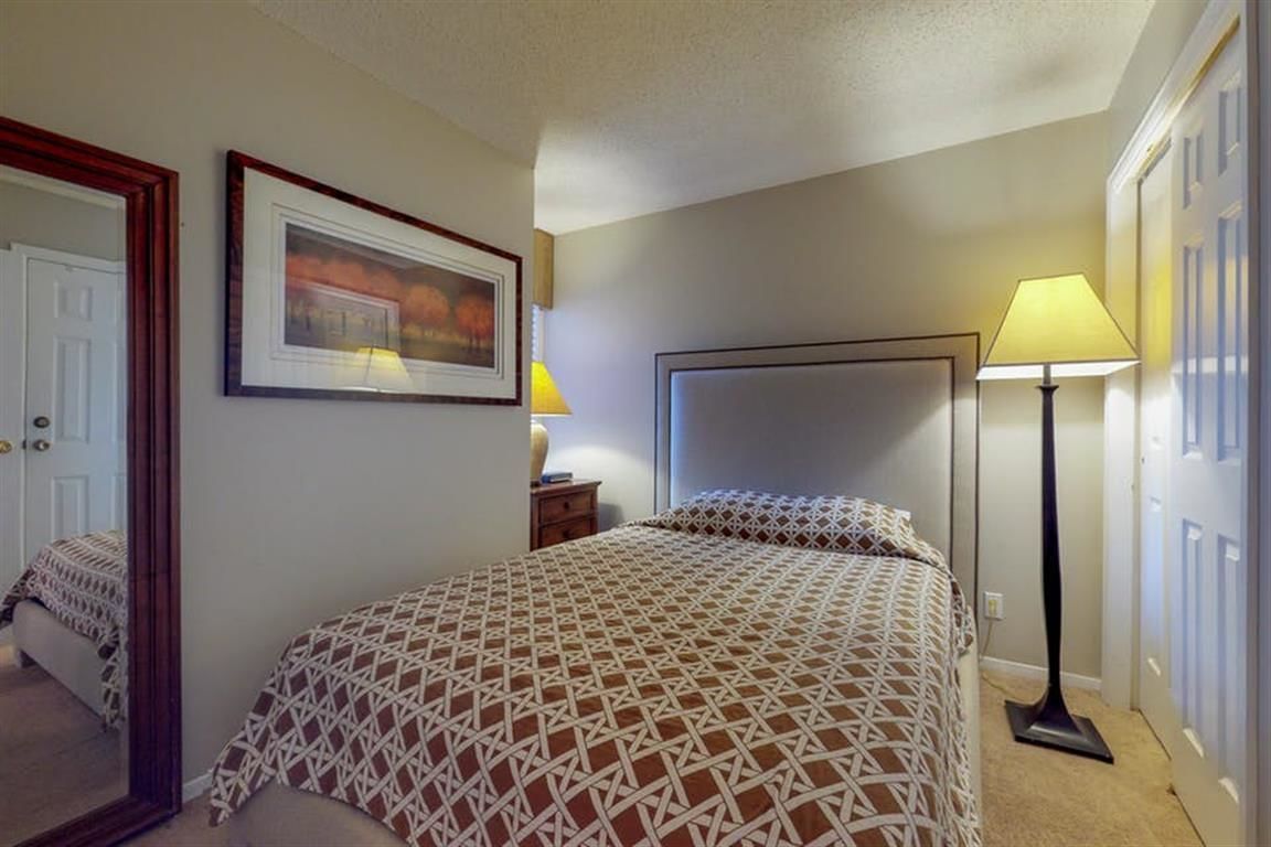 A bedroom with a bed, a nightstand, a lamp, a framed picture, and a door.