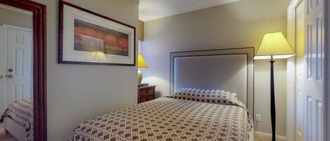 A bedroom with a bed, a nightstand, a lamp, a framed picture, and a door.