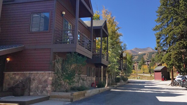 A two-story building with a balcony, stone foundation, and a view of mountains in the background. - Wildwood Lodge Downtown Condos with Hot Tub (Breckenridge)
