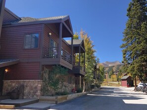 A two-story building with a balcony, stone foundation, and a view of mountains in the background.