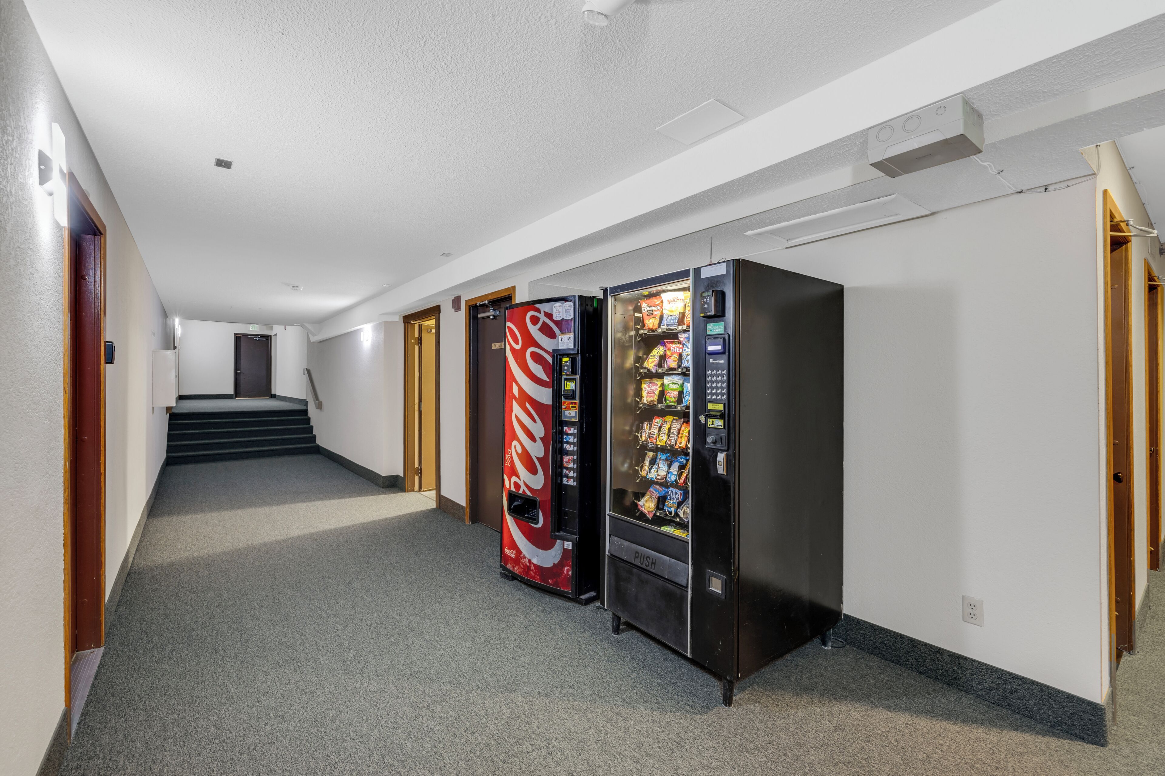 A hallway with vending machines, a staircase, and doors.
