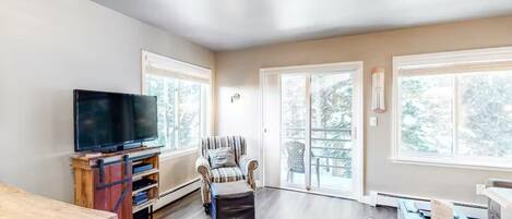 A spacious living room with a flat-screen TV, a striped armchair, and a wooden table.