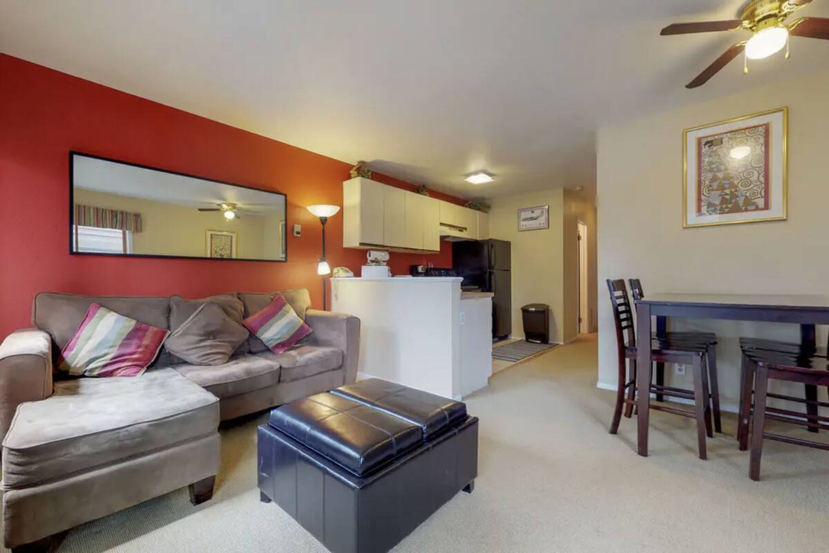 A living room with a sofa, ottoman, and a dining area with a table and chairs.