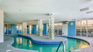 Een binnenzwembad met helderblauw water, omringd door blauwe wanden en kolommen met groene plantmotieven.