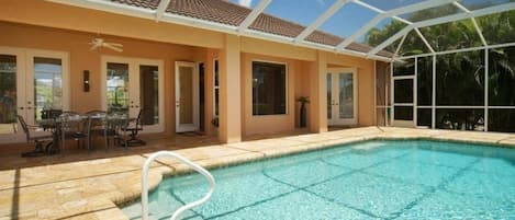 Ein Schwimmbad mit Glasdach, umgeben von einer Terrasse mit Gartenmöbeln.