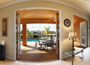 A room with a glass door leading to a pool area, a table with chairs, and a lamp on a glass table.