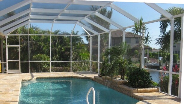 A covered swimming pool with a clear view of palm trees and a house in the background. - Bahama by 123cape VR (Cape Coral)