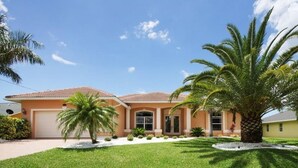 A two-story house with a red-tiled roof, a front garage, and a well-maintained lawn with palm trees. - Bahama by 123cape VR (Cape Coral)