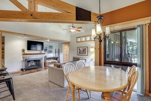 A spacious living area with a fireplace, a dining table, and a large window offering a view of the outdoors.