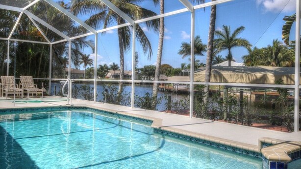 A swimming pool with a covered area, palm trees, and a view of a body of water. - American Dream by 123cape VR (Cape Coral)