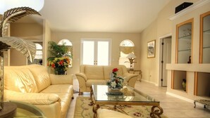 A living room with a beige sofa, a glass coffee table, and a floral rug. - American Dream by 123cape VR (Cape Coral)