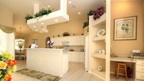 A modern kitchen with white cabinetry, a central island, and a dining area with a wooden table and chairs. - American Dream by 123cape VR (Cape Coral)