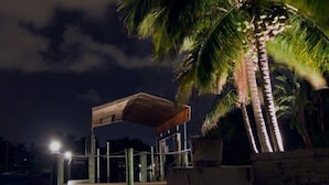 A nighttime scene with a palm tree and a covered structure, possibly a gazebo or pavilion, under artificial lighting. - American Dream by 123cape VR (Cape Coral)