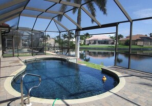A covered swimming pool with a clear view of the surrounding area, including a body of water and distant buildings. - Splendor by 123cape VR (Cape Coral)