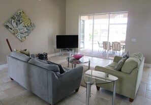 A living room with two sofas, a flat-screen TV, a glass coffee table, and a dining area with chairs and a table. - Splendor by 123cape VR (Cape Coral)