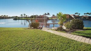 A serene lakeside view with a well-maintained lawn, a small bridge, and a building with a glass facade.