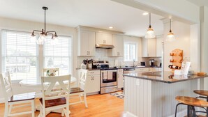 A modern kitchen with white cabinetry, a central island, and pendant lighting. - Walk to Pawcatuck River: Family-Friendly Home! (Pawcatuck)