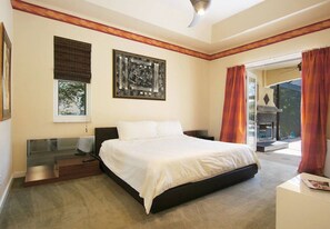 Een slaapkamer met een bed, een nachtkastje, een raam met zonwering, een schilderij aan de muur en uitzicht door het raam.