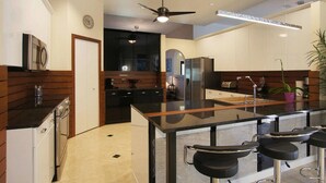 A modern kitchen with a central island, bar stools, and a ceiling fan. - Country Club Residence by 123cape VR (Fort Myers)