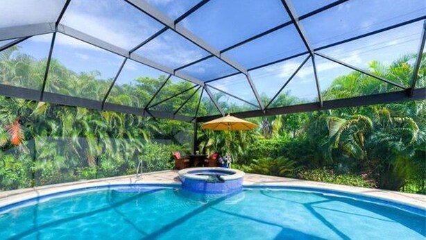 An indoor swimming pool with a glass ceiling, surrounded by lush greenery. - Country Club Residence by 123cape VR (Fort Myers)