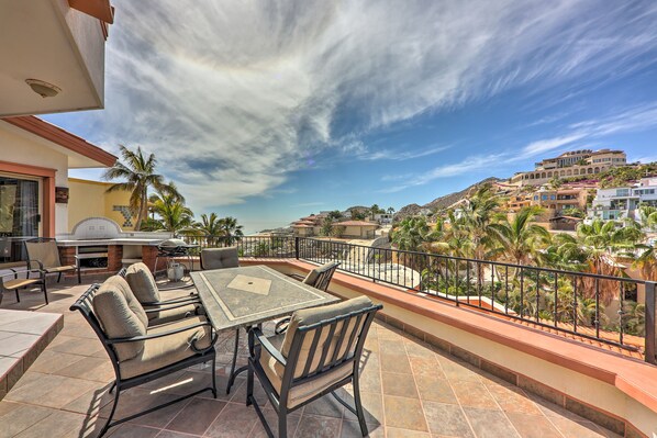 Une terrasse avec une table et des chaises, un barbecue et une vue sur les palmiers et les bâtiments.