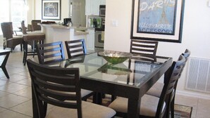 A dining area with a glass-top table surrounded by chairs, a kitchen in the background, and a framed picture on the wall. - Yvonne by 123cape VR (Cape Coral)