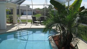 A pool with a glass enclosure, surrounded by chairs and palm trees. - Yvonne by 123cape VR (Cape Coral)